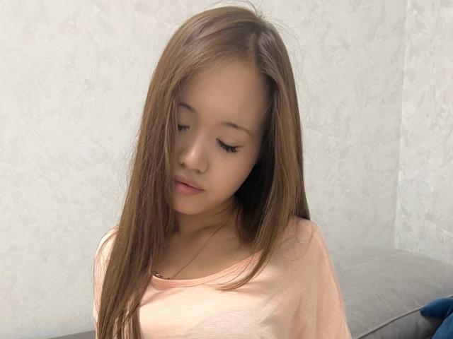 HotyAsianLunachka has long brown hair, closed eyes, and a slight smile, wearing a pink shirt, with a soft, cute face, and a small, delicate nose.