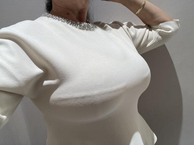 DeesseBleue's white dress with puffed sleeves, showing her tits, has a sparkly collar. She's wearing a gold bracelet, her arm raised. Sunlight casts shadows on her chest.