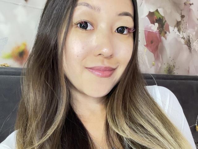 RenyLime has light brown skin, long straight brown hair with blonde highlights, and pink lipstick. She's smiling slightly with pink eyelashes, wearing a white top.