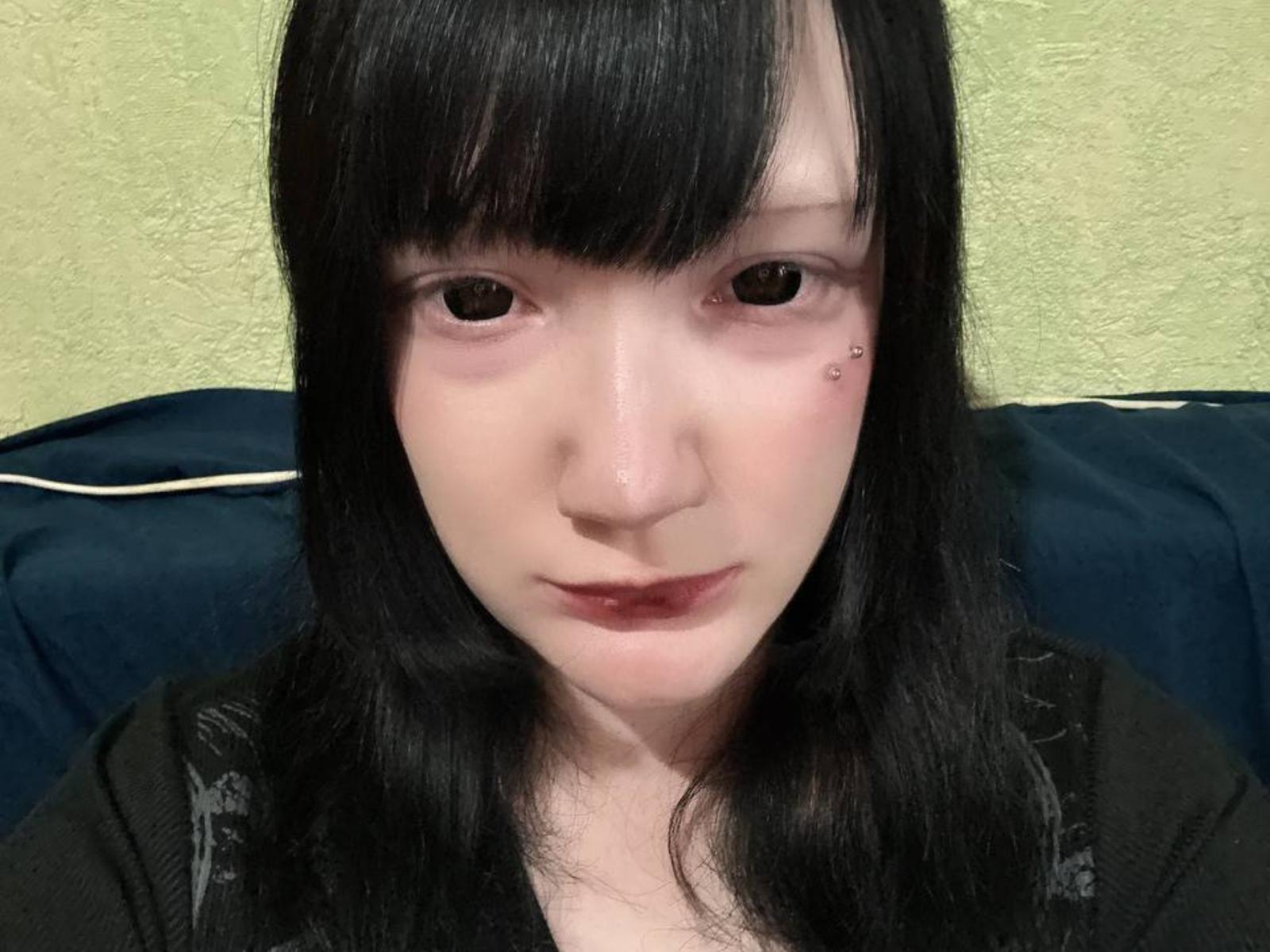 HongColclasure ha la pelle chiara, capelli neri e lisci con frangia, occhi marroni, una piccola cicatrice sul viso e indossa una maglietta nera, con le labbra leggermente rosate..
