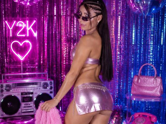 LeiaLaurent has long black braids, wears sunglasses, a shiny pink bra, and a matching mini skirt, showing her ass, holding pink fluff, with a pink purse and radio.