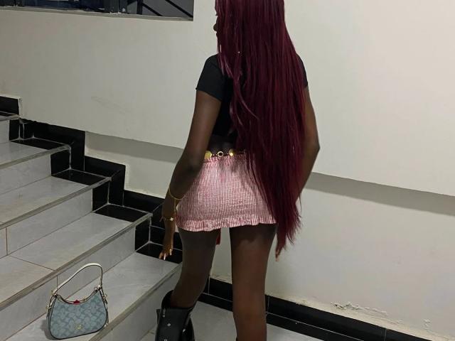 EbonySweet-hot with long red hair, black top, pink checkered mini skirt, black boots, standing on stairs, hand on wall, small blue purse on step.