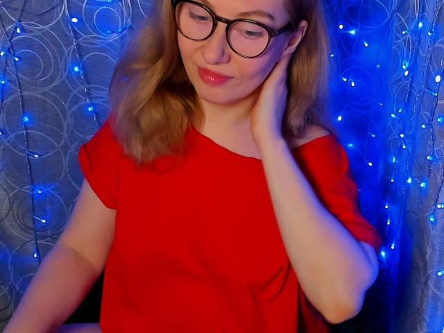 PaulinaSunny with glasses, red dress, blonde hair, hand on cheek, blue fairy lights in background, smiling gently, cute, soft lighting.