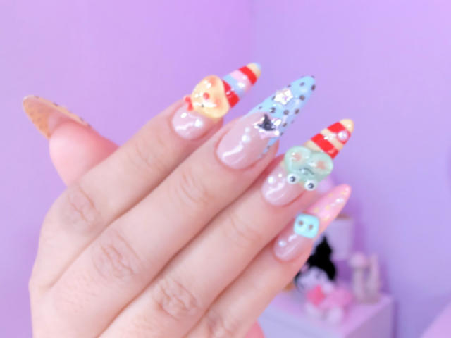 MarlaBriard's boofed nails are long with colorful, detailed designs: candy striped, blue with dots, green frog, and yellow with a face. Her nails are glossy and well-manicured.