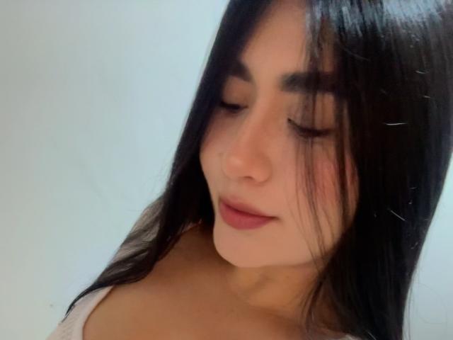 MiaDuboisX has long black hair, closed eyes, and a subtle smile, with her bare shoulders visible, showing her soft skin and pink lipstick.