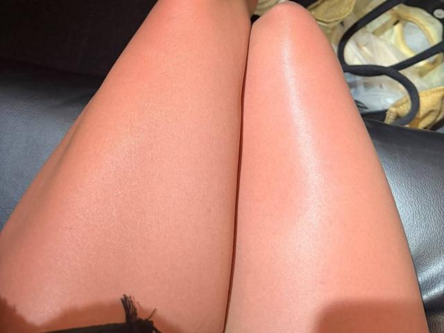 ChristieGarci's shiny, smooth, tan thighs are prominently displayed, with a small black hair follicle visible at the bottom, on a dark leather surface.