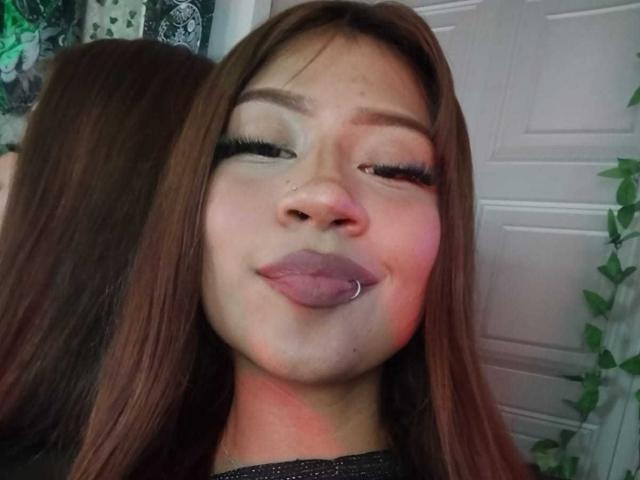 BonnieBodn met bruin haar, gesloten ogen, roze lippen, tong uit, neusring en lange wimpers, gekleed in een zwarte top, op een selfie..
