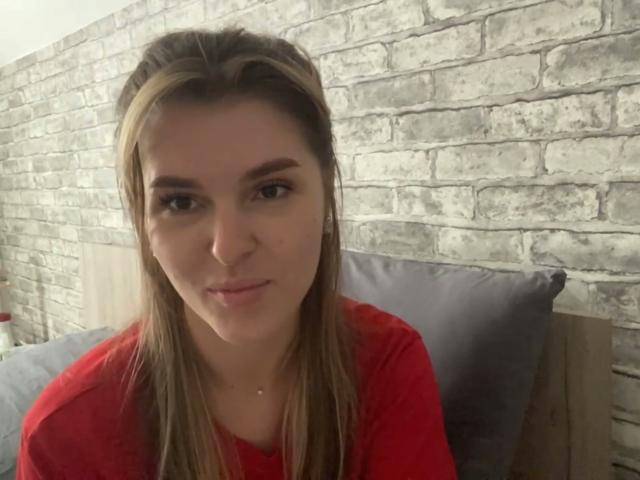 Elana Falencki tiene el cabello castaño lacio, una camisa roja y una sonrisa discreta. Se pueden ver sus ojos marrones y su piel clara. Está sentada apoyada en almohadas grises sobre una cama de madera..