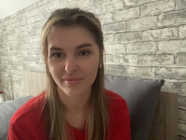 ElanaFalencki has straight brown hair, a nose ring, and is wearing a red shirt, sitting with a slight smile, looking at the camera. Her tits are small and cute.