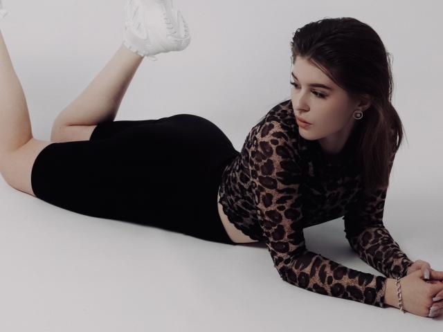 Elana Falencki è sdraiata a pancia in giù, indossa una maglietta a stampa leopardo e pantaloncini neri, con scarpe da ginnastica bianche, ha il sedere sollevato e guarda di lato. Ha degli orecchini e un braccialetto..