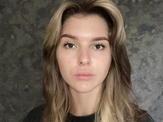 Elana Falencki ha i capelli biondo-castani, mossi, gli occhi verdi e un viso serio con labbra leggermente rosate. Indossa una maglietta nera e i suoi glutei non sono visibili..