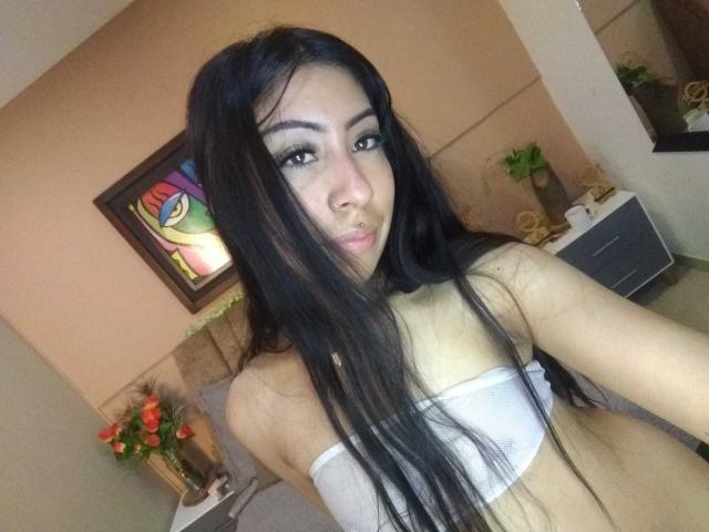 LinaSpearce with long black hair, wearing a white strapless top, showing her small tits and nose ring, looking at the camera with a slight pout.