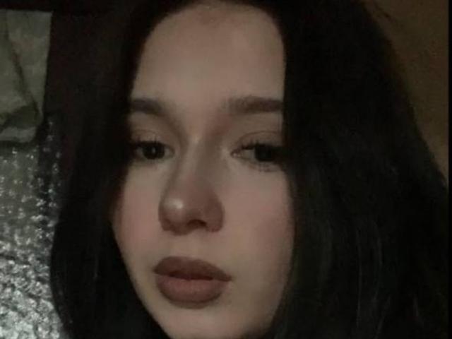 CarriMey hat dunkles, welliges Haar, blasse Haut und volle, braune Lippen. Sie trägt dezentes, natürliches Make-up und hat einen leicht ernsten Gesichtsausdruck. Ihre kleinen, dunklen Augen sind halb geschlossen..