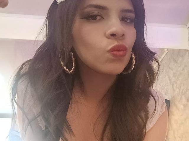 VioletaStone pouting her full, pink lips with dark, wavy hair and wearing large, gold hoop earrings. Her eyes are lined with black eyeliner. She's in a soft light.