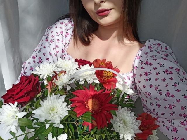 MissCourtney with a bouquet of red and white flowers, wearing a floral-patterned dress, has red lips and dark brown hair, showing her tits and the flowers in front.