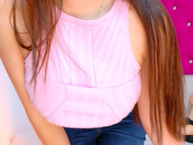 FreyaraVenwo's pink ribbed sleeveless top with a subtle V-shaped pattern, showing her small boobs and long brown hair, wearing dark blue jeans.