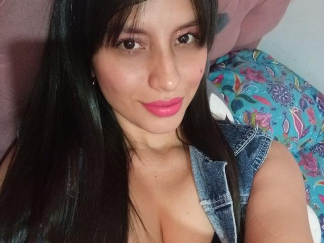 MadissonFontaine, com cabelo preto, batom rosa e blusa de jeans, aparece em um selfie mostrando seus seios, sorrindo para a câmera. Seus olhos são castanhos e ela tem um rosto bonito..