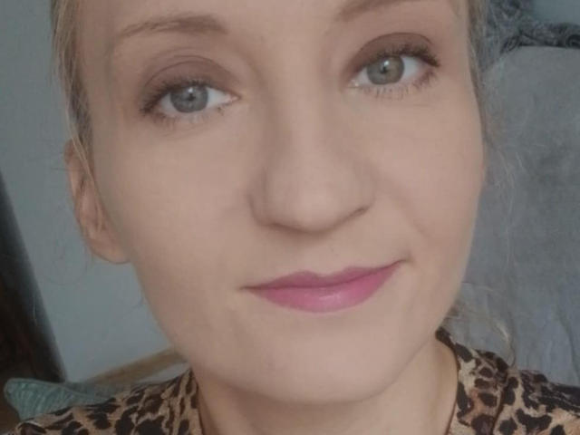 ViolettaLoves has blue eyes, pink lipstick, and a light skin tone, with blonde hair and a leopard print shirt, smiling softly at the camera.
