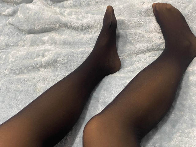 JessikaBernskoetter's legs, covered in black sheer pantyhose, are lying on a white textured blanket, with her feet slightly pointed and toes touching.