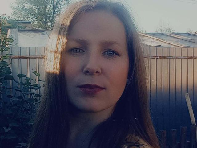 MelodyAmber has light brown hair, fair skin, and blue eyes with red lipstick. She's wearing a green shirt, and a sunbeam is shining on her face.