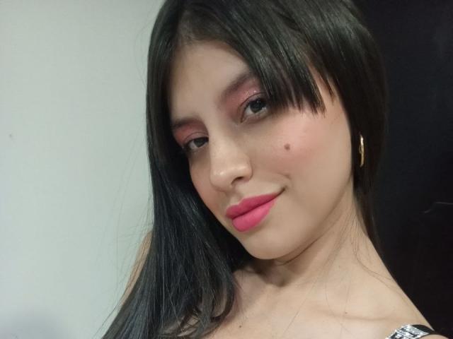 MadissonFontaine with black hair, pink eyelids, pink lips, gold earrings, and a cute nose mole, smiling softly. Boobs not visible, focus on face.
