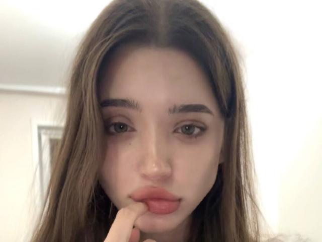 Catina Letchworth, avec ses longs cheveux bruns, ses yeux verts et ses lèvres rosées légèrement entrouvertes, touchant sa lèvre inférieure avec son index droit, regardant directement l'appareil photo..