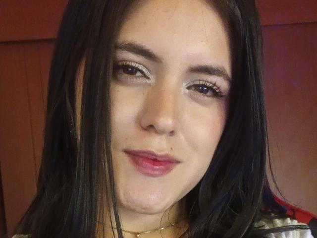 MiaXLovely hat langes, schwarzes Haar, helle Haut und rosafarbene Lippen mit dezentem Make-up. Sie schaut mit einem leichten Lächeln in die Kamera und zeigt ihr süßes Gesicht und ihre Wimpern..