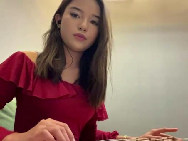 ZulaGullick, con capelli marrone chiaro, rossetto rosa e una camicetta rossa con volant, guarda leggermente di lato con un'espressione neutra, con le mani appoggiate su una superficie..