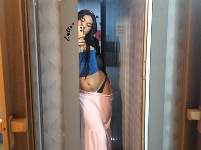 PamelaXFox with long black hair, blue crop top, showing her tan midriff and black thong, pink pants, taking a mirror selfie, holding a gold phone.