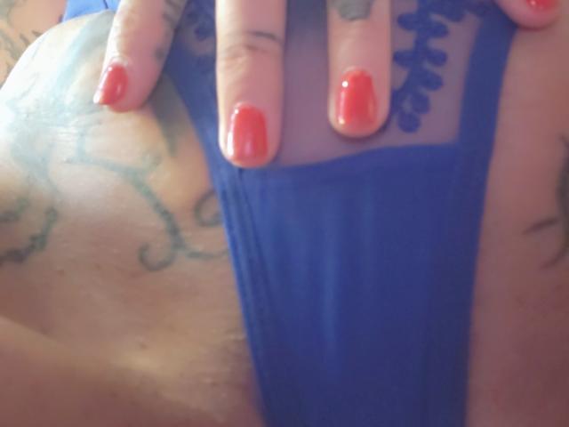FrenchShanna's hand with red nail polish rests on her blue lace panties, showing tattoos on her side and a partially visible tattoo on her fingers.