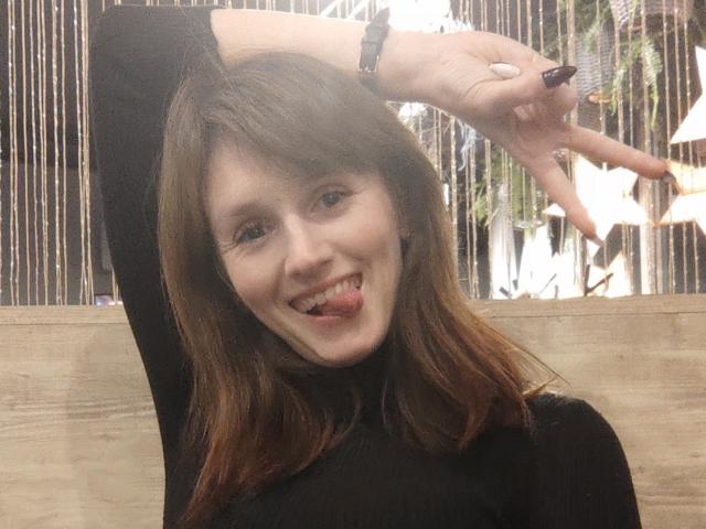 FavoriteHare with brown hair, black turtleneck, tongue out, making a peace sign, smiling, wearing a black wristband, indoors, light skin, cute, medium build, casual selfie.