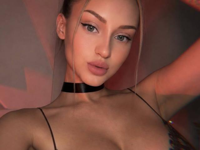 MargertRedFlower with blonde hair, black choker, and eyeliner, looking at camera, her tits barely covered by thin black straps, soft pink lips, and a sexy, confident expression.