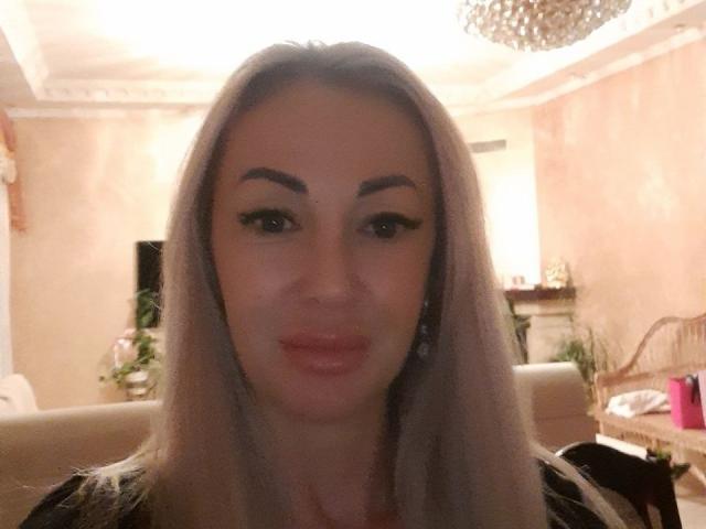 MysteryLaddy ha lunghi capelli biondi, sopracciglia folte e labbra piene di colore rosa. Sta guardando la fotocamera con un leggero sorriso, indossando una maglietta nera con motivi discreti..