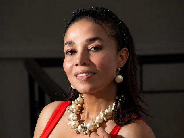 MiaLucchi has brown skin, dark hair, and is smiling with red dress, pearl necklace, and earrings. She's wearing a black headband with sparkles, and has small tits.