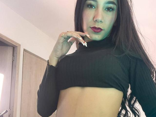 VioletaVelvet with long dark hair, wearing a black ribbed crop top, showing her small tits and toned midriff, with dark red lipstick and a ring on her finger.