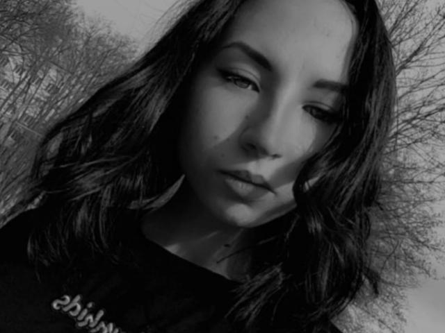 Autoportrait en noir et blanc de VanessaSims, avec des cheveux noirs ondulés, un maquillage discret et une chemise sombre. Elle regarde légèrement vers le bas avec une expression sérieuse, et sa fesse est visible dans l'ombre..