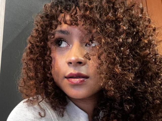 SofiaPassionne has curly brown hair, wide brown eyes looking up, and glossy pink lips. She's wearing a white shirt, looking cute and slightly surprised.