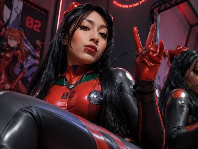 AilenRosse with long black hair, wearing a red and black latex cosplay, showing a peace sign with red-gloved hand, her plump tits and shiny latex suit visible.