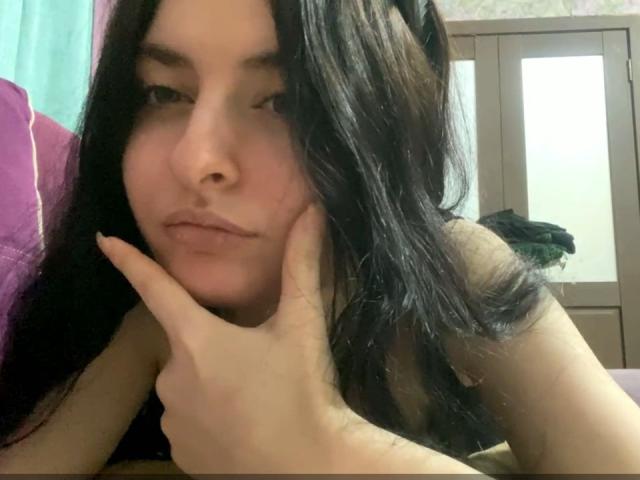 ArceliaWroten with long black hair, pouty lips, and pale skin, resting her chin on her hand, looking into the camera, showing her bare shoulders and a subtle, confident expression.
