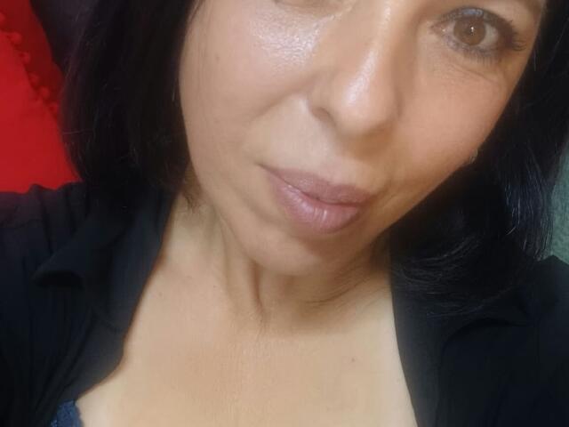 O rosto de LauraSin em uma selfie, mostrando seus olhos castanho-claros, lábios rosados e brilhantes, e pele levemente luminosa. Ela está vestindo uma camisa preta com decote baixo, que revela o colo..