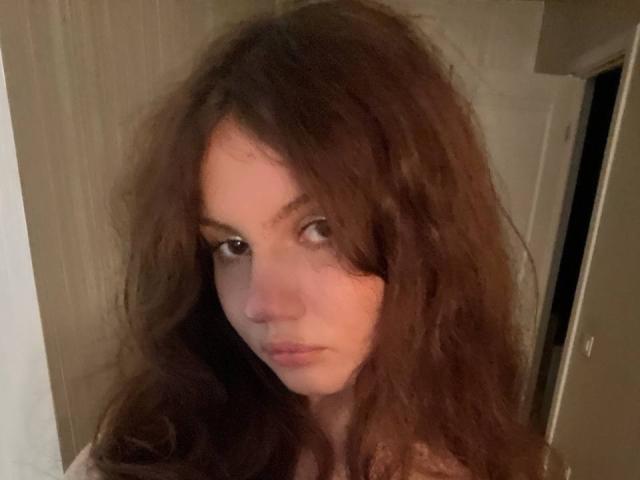 TanaFietek has messy, dark brown curly hair and a serious expression. She's looking slightly to the side with her lips closed. Her nose is small and her eyes are dark.