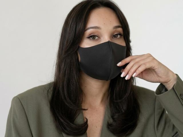 SexLoveG, con capelli castano scuro, indossa una maglietta verde e una maschera nera, toccandosi il mento con le unghie bianche. Ha gli occhi marroni e un'espressione neutra..