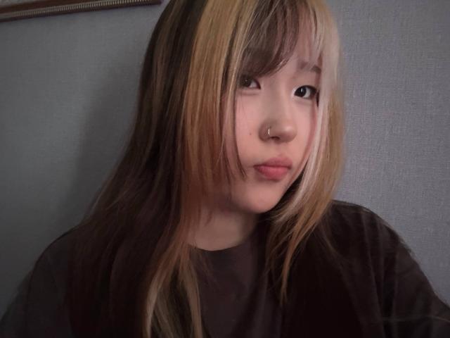 JungMcgranor has long, brown and blonde hair, a nose ring, and is wearing a black shirt, looking slightly bored with pouty lips, in a soft-lit photo.