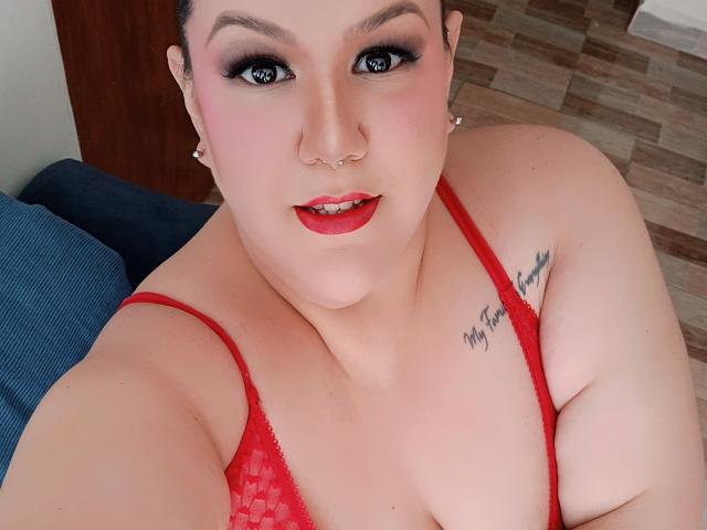 GiiannaMorrys with red lipstick, red bra, nose ring, and tattoo on right shoulder. She's smiling, showing her tits, and has dark makeup. Her skin is fair.
