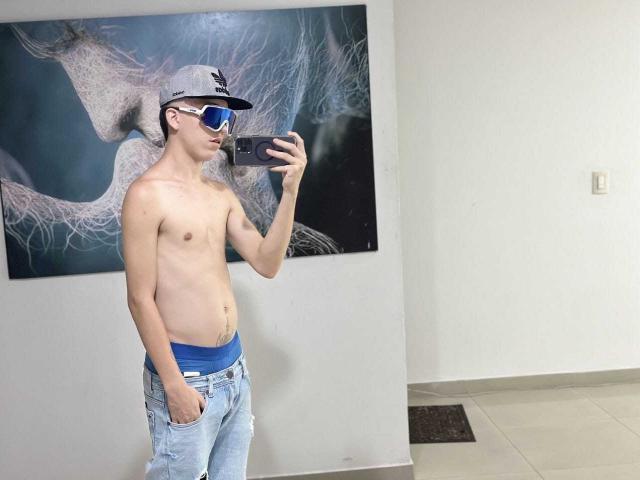 Shirtless SantiagoColeman with a slim build, blue underwear, and jeans, wearing a cap and sunglasses, taking a mirror selfie. His hand is in his jeans' pocket.