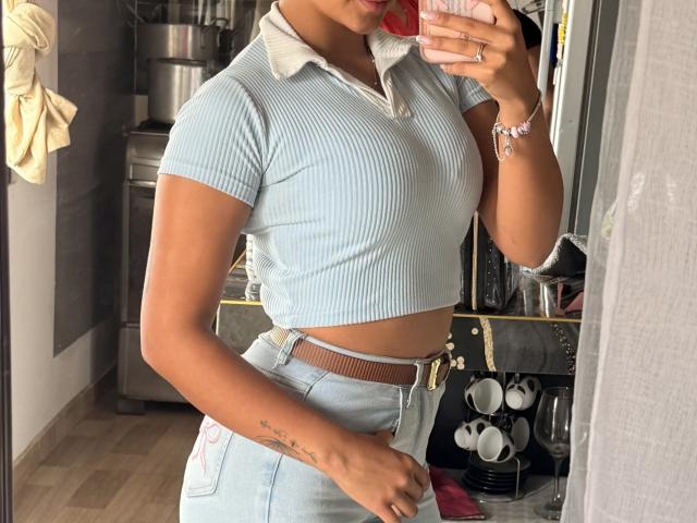 SarahPrincess in a ribbed, light blue, short-sleeve crop top, showing her small tits and slim waist, with high-waisted, light blue jeans and a brown belt.