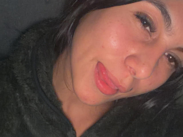 SarahPrincess with pouty red lips, slightly flushed cheeks, and dark eyebrows, wearing a black fuzzy sweater, has short black hair, and is looking at the camera.