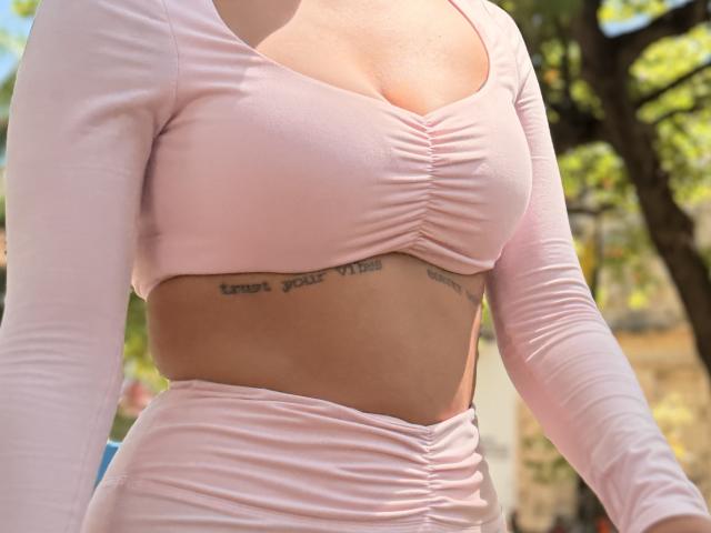SarahPrincess has pale pink, ruched, long-sleeve top showing her tits and tattoo under her boobs. She's wearing a matching pale pink, ruched, high-waisted bottom.