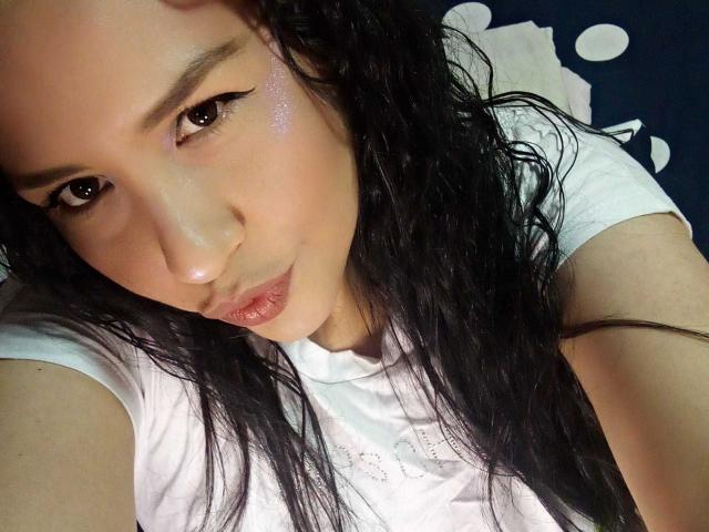 MarySweett69, com cabelo preto molhado, lábios rosados e delineador, vestindo uma camisa branca, olhando para a câmera com uma expressão ligeiramente alegre..