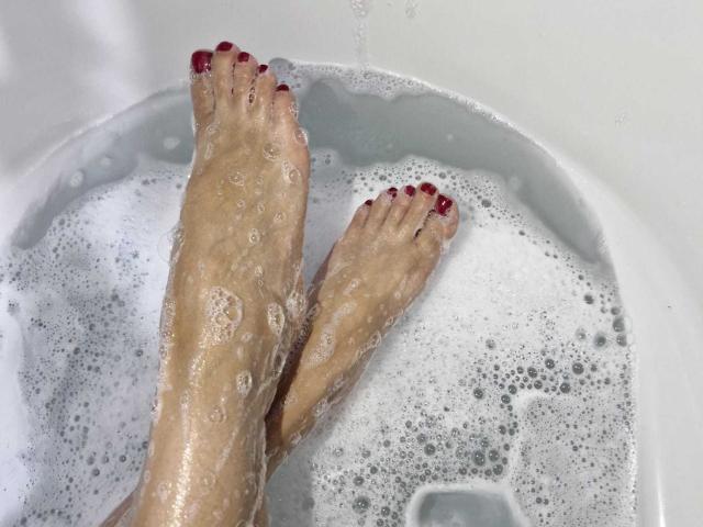 KammyJoe's soapy feet with red-painted toenails in a white bathtub, bubbles covering skin, water droplets, and a soap suds pattern.